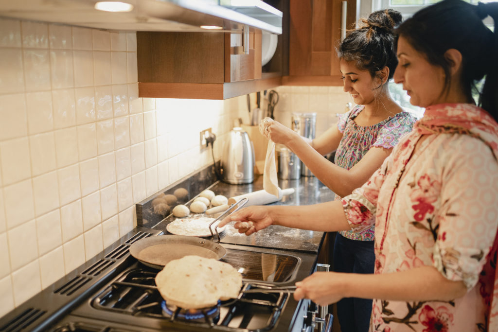 Mother and daughter cooking chapattis on the stove.